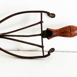 May include: A vintage, rusty metal clothes iron with a wooden handle. The iron has a curved shape and a pointed end. The handle is brown and has a knob at the end.