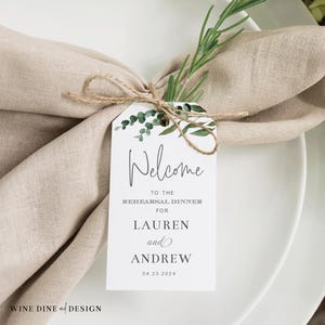 May include: White card with green foliage design. Text reads "Welcome to the Rehearsal Dinner for Lauren and Andrew 04.23.2024".
