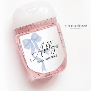 K&ouml;nnte beinhalten: Eine durchsichtige Plastikflasche mit einer blauen Schleife und dem Text "Ashley's Baby Shower" auf einem wei&szlig;en Etikett.