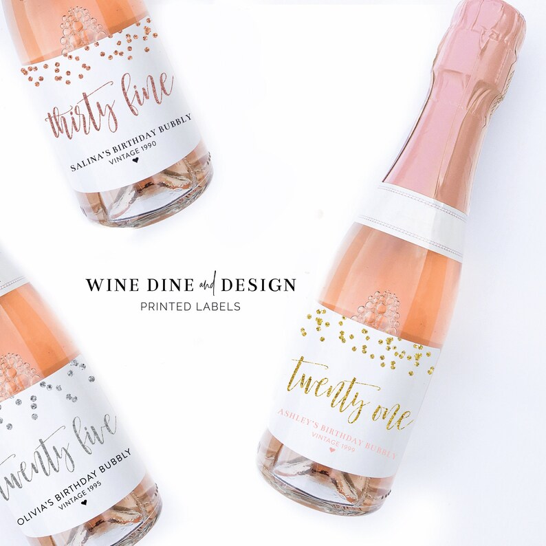 May include: Three mini champagne bottles with personalized labels. The labels are white with gold confetti and black calligraphy. The labels read "thirty fine", "twenty one", and "twenty five". Each label includes the person's name, the occasion, and the year.