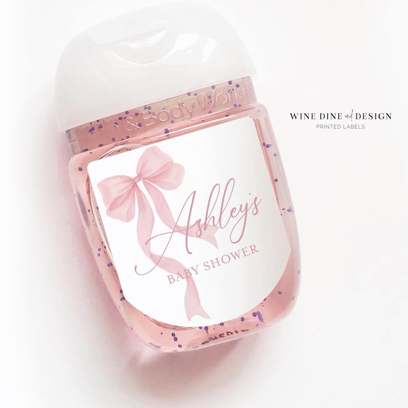 K&ouml;nnte beinhalten: Eine durchsichtige Plastikflasche mit einem wei&szlig;en Pumpspender und einem rosa-wei&szlig;en Etikett. Das Etikett zeigt eine rosa Schleife und den Text "Ashley's Baby Shower".