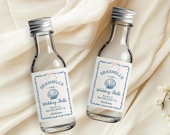 Op de afbeelding: Twee kleine, heldere glazen flesjes met zilveren doppen. Elk flesje heeft een wit etiket met blauwe geschulpte randen, de woorden "Seashells and Wedding Bells" en een schelpgrafiek. De tekst "Riley's Bachelorette Charleston" staat ook op het etiket.