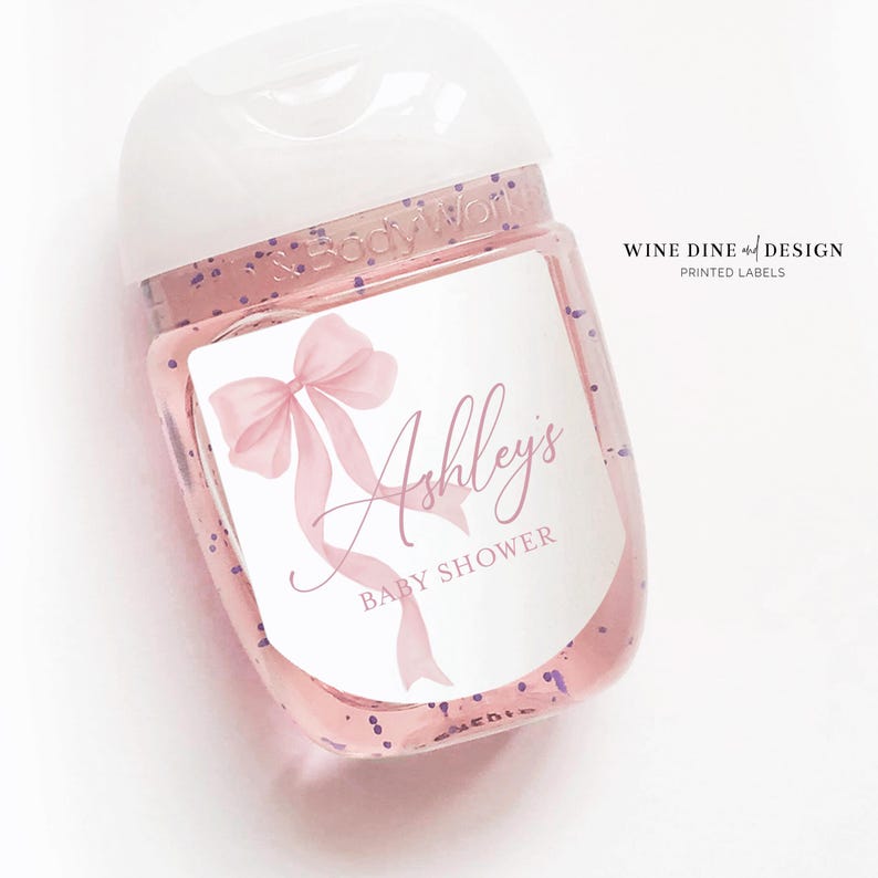 K&ouml;nnte beinhalten: Eine durchsichtige Plastikflasche mit einem wei&szlig;en Pumpspender und einem rosa-wei&szlig;en Etikett. Das Etikett zeigt eine rosa Schleife und den Text "Ashley's Baby Shower".