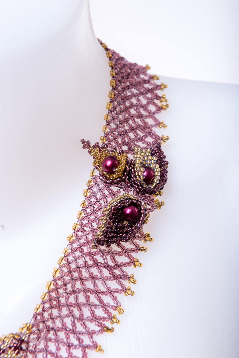 May include: A delicate beaded necklace with a geometric pattern and a floral design featuring purple and gold beads.