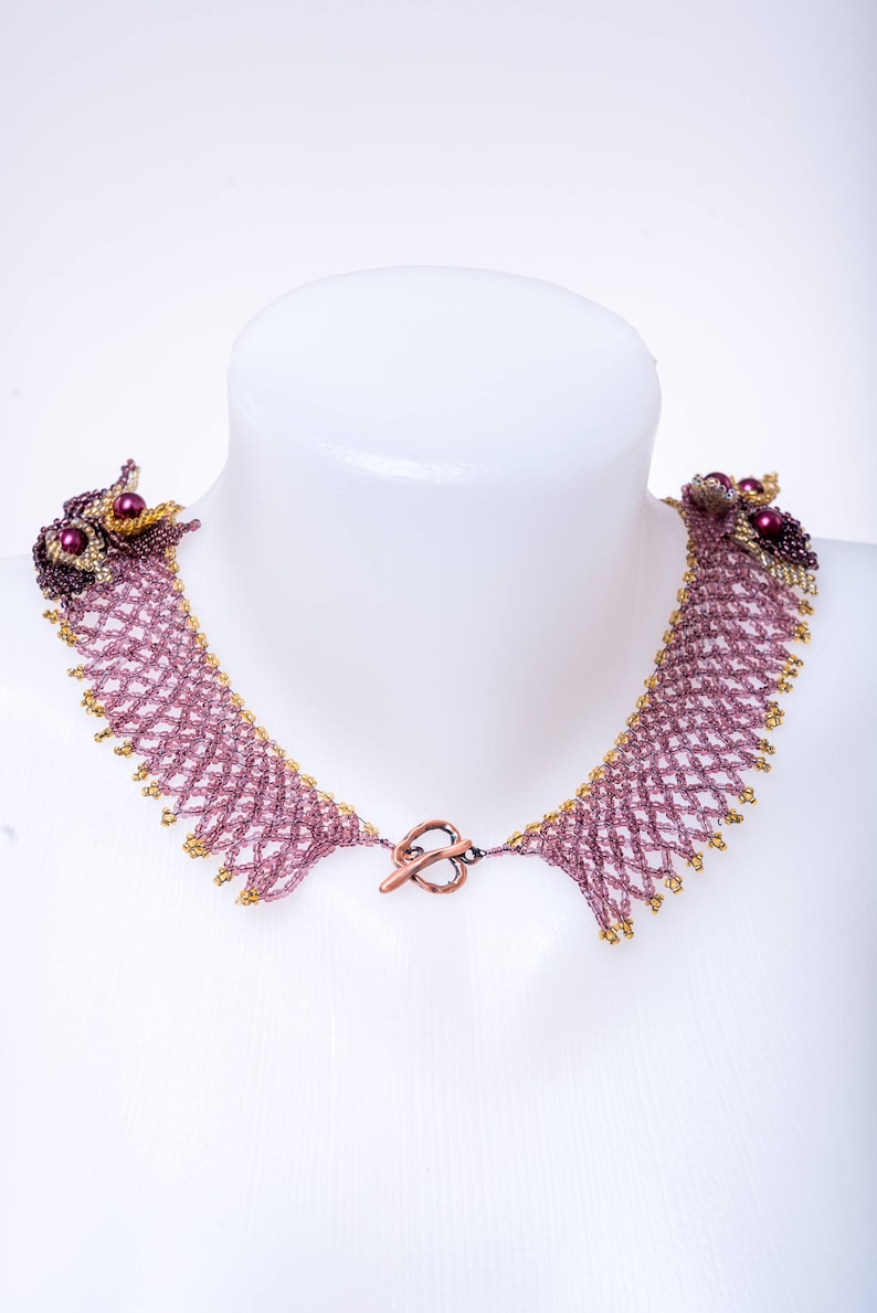 May include: A delicate beaded necklace with a copper clasp. The necklace is made of small, purple and gold beads woven into a intricate pattern.