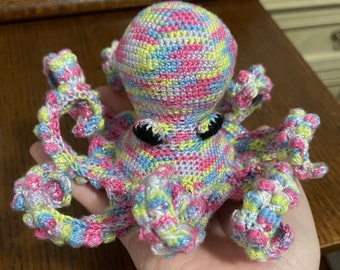May include: A crocheted octopus toy with a pink, blue, yellow, and white striped pattern. The octopus has eight tentacles and black eyes.