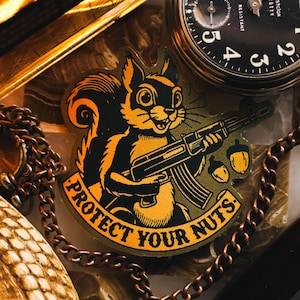 May include: A sticker featuring a cartoon squirrel holding an assault rifle with the text "Protect Your Nuts." The sticker is on a brown background with a chain and a pocket watch.