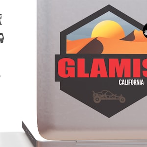Puede incluir: Una pegatina negra y naranja con una puesta de sol sobre dunas de arena y el texto "Glamis California". Una silueta de un buggy de dunas se encuentra debajo del texto. La pegatina tiene una forma hexagonal negra con un borde blanco.