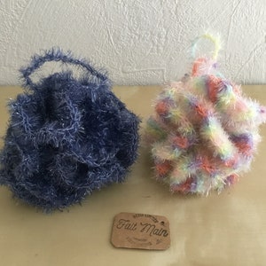 Peut inclure: Deux poufs de bain en crochet faits main. L'un est bleu avec une finition scintillante et l'autre est un arc-en-ciel de couleurs. L'étiquette indique "Fait Main".