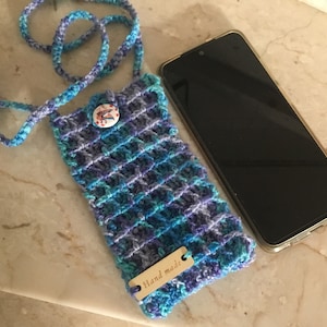 May include: A crocheted phone case with a blue and purple color scheme. The case has a small button and a tag that says "Hand made".