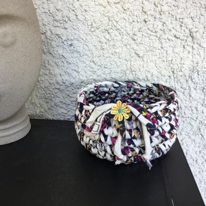 Peut inclure: Un petit panier rond tissé à partir de chutes de tissu. Le panier est noir, blanc et rose avec un accent de fleur jaune.
