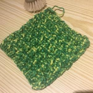 Puede incluir: Un paño de cocina o estropajo de ganchillo verde y amarillo. El paño es de forma cuadrada y tiene una superficie texturizada.