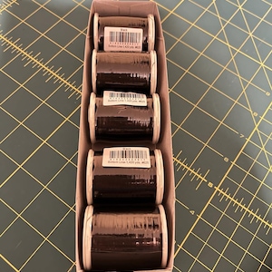 May include: Six spools of black thread in a cardboard box. Each spool has a label that reads "Bottom Line - 1,420 yds. #125".