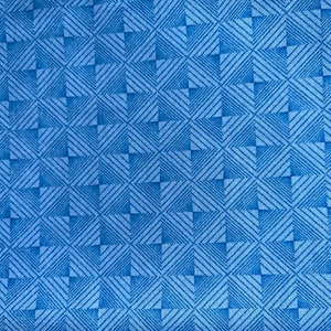 May include: A close-up of a blue fabric with a geometric pattern. The design features squares and diagonal lines in varying shades of blue, creating a textured appearance. The fabric appears to be woven.