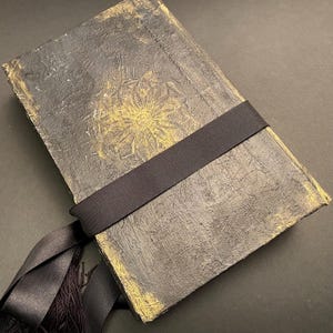 May include: A black journal with a gold embossed floral design and a black ribbon closure.