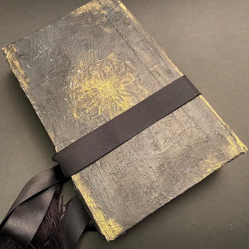 May include: A black journal with a gold embossed floral design and a black ribbon closure.
