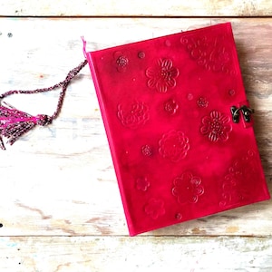 May include: A bright pink journal with embossed floral designs and a metal clasp. The journal has a beaded tassel attached to the spine. The cover is a vibrant shade of pink.