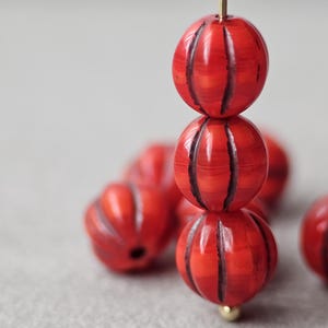 May include: A close-up of red and black striped round beads. The beads are made of a smooth, glossy material and have a slightly textured surface.