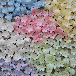May include: A selection of translucent flower-shaped beads in pastel shades of pink, blue, yellow, green, and white. The beads are scattered, displaying their delicate, petal-like design. These beads are suitable for jewellery making and craft projects.