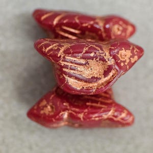 May include: Three red ceramic fish charms with gold accents. The fish are stacked on top of each other.