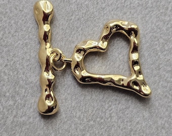 May include: Gold-toned metal heart-shaped toggle clasp with a textured surface. The clasp has a bar that slides through the heart.
