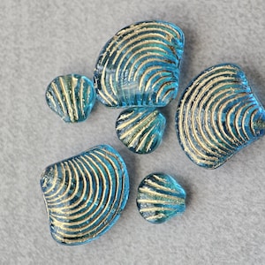May include: A collection of six blue glass seashells with gold accents. The shells are all different sizes and shapes, and they have a textured surface.