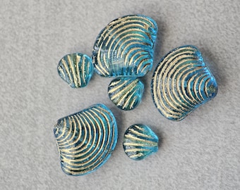 May include: A collection of six blue glass seashells with gold accents. The shells are all different sizes and shapes, and they have a textured surface.