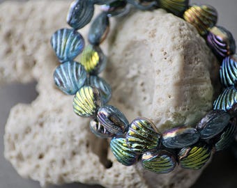 May include: A strand of iridescent blue and green glass beads with a ribbed texture. The beads are teardrop-shaped and are resting on a piece of white coral. The beads have a metallic sheen.