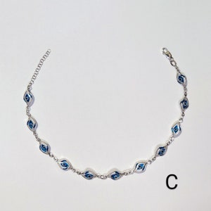 K&ouml;nnte beinhalten: Silberfarbenes Fu&szlig;kettchen mit einer Reihe von blau-wei&szlig;en Evil-Eye-Anh&auml;ngern. Die Anh&auml;nger sind oval und mit einem detaillierten Augendesign versehen. Das Fu&szlig;kettchen hat eine filigrane Kette und einen Verschluss. Der Buchstabe "C" ist unten rechts zu sehen.