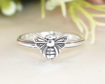 May include: A silver ring with a bee design. The bee is detailed with wings, a body, and legs.