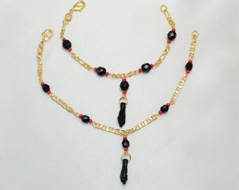 May include: Two gold-colored chain bracelets and a necklace. Each piece features black and red beads, with a black hand pendant. The jewelry is displayed on a white surface.