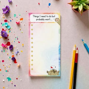 May include: A notepad with a rainbow gradient background and the text "Things I need to do but probably won't..." is displayed at the top. The notepad features a cat graphic and star icons. Coloured pencils and a succulent plant are also visible.