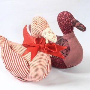May include: Two handmade fabric toy ducks. One duck is red and white gingham with a red bow. The other duck is pink and purple paisley with a brown beak.