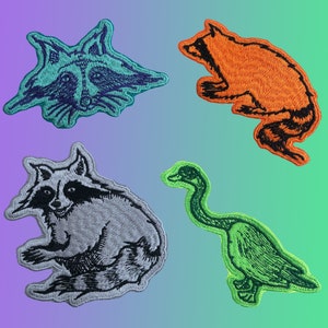 May include: Four embroidered iron-on patches featuring a raccoon, a goose, and two different styles of raccoons. The patches are in various colours, including green, orange, black, and grey.
