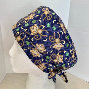 May include: A blue scrub hat with a pattern of brown monkeys swinging from vines with yellow bananas and green leaves.