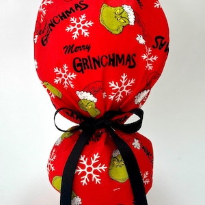 May include: Red scrub cap featuring a Grinch and snowflake pattern with the words "Merry Grinchmas." The cap is tied with a black ribbon. The cap is designed for medical professionals.