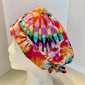 May include: A colorful tie-dye surgical scrub hat with a bright orange, pink, blue, green, and purple pattern. The hat is tied at the back with a bow.