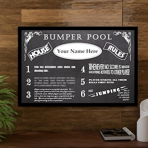 May include: Black and white chalkboard sign with the title "Bumper Pool" and rules for the game. The rules include: "Coin toss determines color choice and shooting side", "Both players shoot spotted cue ball at the same time toward opposite scoring hole. Shots must hit cushion on player's right side of table", "Whenever no score is made shooting rotates to other player", "Player sinking all their balls first wins", "No jumping - balls over balls or bumpers in banking shots".