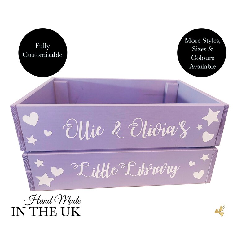 May include: A lilac-colored wooden crate with the words "Ollie & Olivia's" and "Little Library" in white script. The crate is decorated with white hearts and stars. Text on the crate says "Hand Made IN THE UK" and "Fully Customisable".