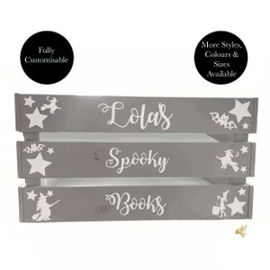 May include: A gray wooden crate with three shelves, featuring white text and Halloween-themed illustrations. The top shelf reads "Lola's", the middle "Spooky", and the bottom "Books". White stars, bats, and witch silhouettes decorate the crate.