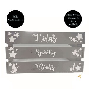 May include: A gray wooden crate with three shelves, featuring white text and Halloween-themed illustrations. The top shelf reads "Lola's", the middle "Spooky", and the bottom "Books". White stars, bats, and witch silhouettes decorate the crate.