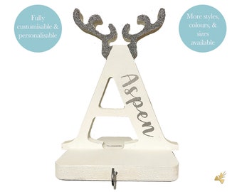 May include: A white wooden shelf in the shape of the letter "A" with silver glitter antlers. The name "Aspen" is written in silver script. The shelf has a small hook and the text "Fully customisable & personalisable" and "More styles, colours, & sizes available".