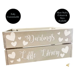 May include: A two-tiered, light gray wooden crate with white heart accents. The top tier reads "Darling's" and the bottom tier reads "Little Library" in cursive. The crate is designed for storage and organization.