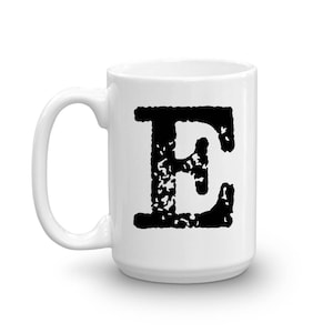 May include: White ceramic mug with a black letter "E" printed on the front. The letter is in a vintage, distressed style.