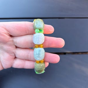 May include: A jade bracelet with green and orange beads. The jade beads are carved with a design.