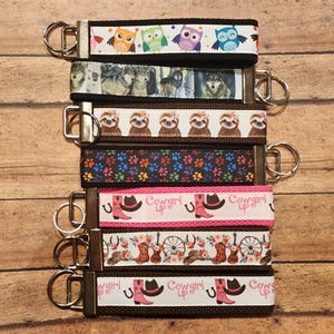 May include: Seven colorful keychains with different designs. The keychains feature owls, wolves, sloths, paw prints, cowboy boots, and floral patterns. Each keychain has a silver key ring.