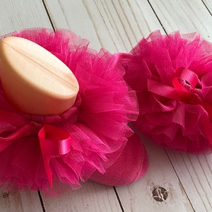 May include: A pair of pink tulle baby socks with a pink satin bow on each sock.