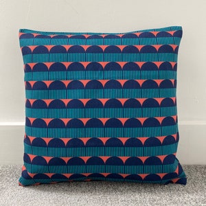 May include: A teal and coral patterned cushion with a geometric design. The cushion is made of a soft, woven fabric.