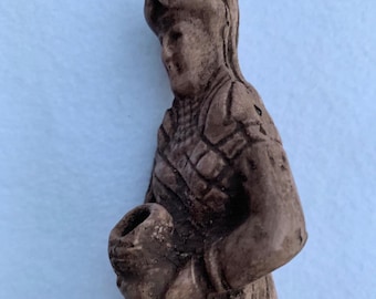 May include: A brown ceramic figurine of a person wearing a hat and holding a round object in their hand.