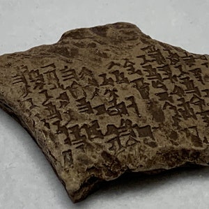 May include: A brown clay tablet with cuneiform script. The tablet is rectangular with rounded edges and has a rough texture. The script is carved into the surface of the tablet.